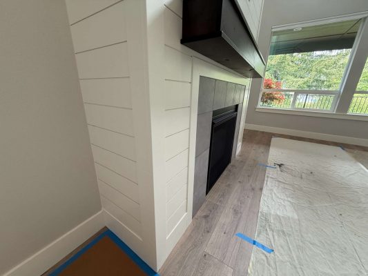 A modern fireplace with white shiplap, gray tile, and a black insert in Portland is prepped with protective sheets and painter’s tape for finishing by Turk of Pearl Painters in May 2025.