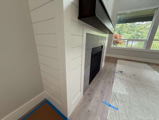 A modern fireplace with white shiplap, gray tile, and a black insert in Portland is prepped with protective sheets and painter’s tape for finishing by Turk of Pearl Painters in May 2025.