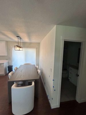 A dining area in Portland features a wooden table, six white chairs, and a modern light fixture. Blue painter's tape marks are visible on the wall, possibly for Pearl Painters' painting work. A partially open door leads to an Arnold-style bathroom.