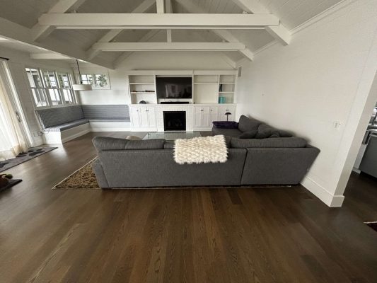 A painter in Portland, inspired by Duffy’s designs, created a timeless living room with a gray sectional sofa, white built-in cabinet and fireplace, wooden floors, and a vaulted white ceiling with exposed beams. Pearl Painters can achieve similar painting results.