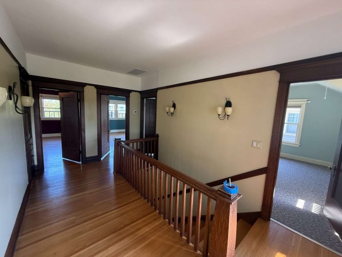 Second-floor hallway with wood floors and trim, wall-mounted lights, and multiple doorways in the Dennis home, Portland. Painted by Pearl Painters as of May 2025.