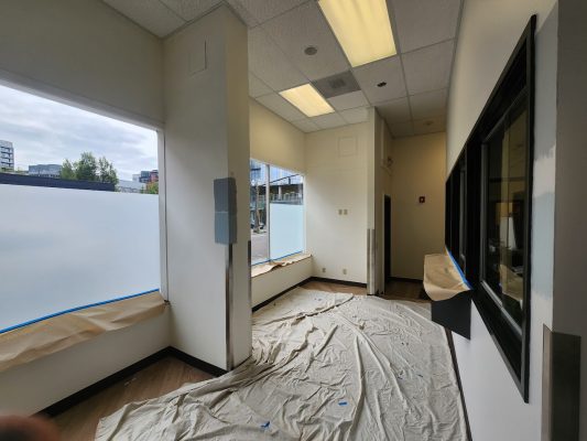 Pearl Painters, a Portland painting company, is preparing an empty office for new tenants with drop cloths and wall protection. The space, filled with natural light from large windows, will be available in June 2025 with Jones INT.