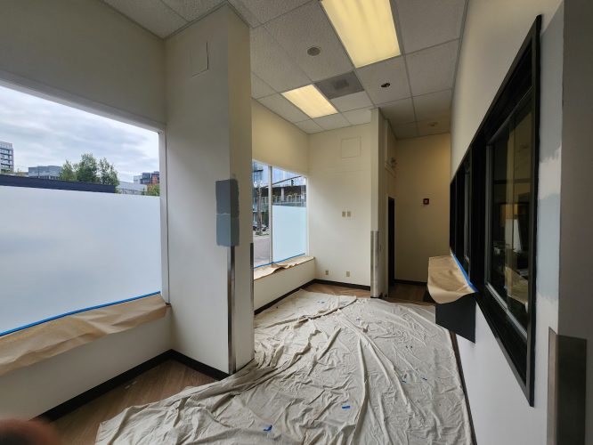 Pearl Painters, a Portland painting company, is preparing an empty office for new tenants with drop cloths and wall protection. The space, filled with natural light from large windows, will be available in June 2025 with Jones INT.