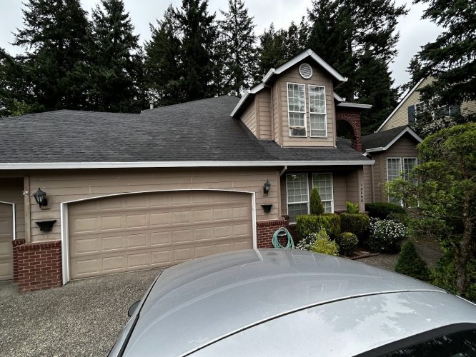 A two-story suburban house in Portland with beige siding, brick accents, and a double garage is shown. Painted by Pearl Painters, the painting captures the home’s exterior amid shrubs and trees in June 2025.