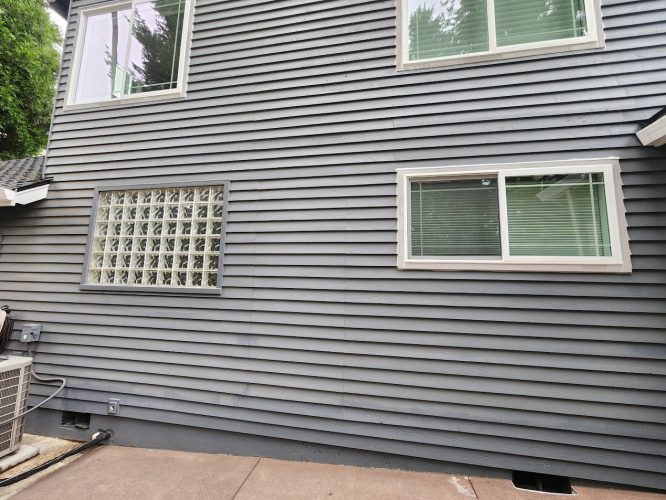 Gray-striped house with two windows, one glass block window, A/C unit. Painted by Pearl Painters, Portland. July 2025.