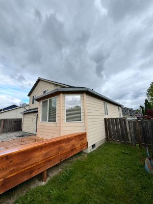 A beige house with white trim, located in Portland, has a fenced backyard and wooden deck. Painted by Pearl Painters.