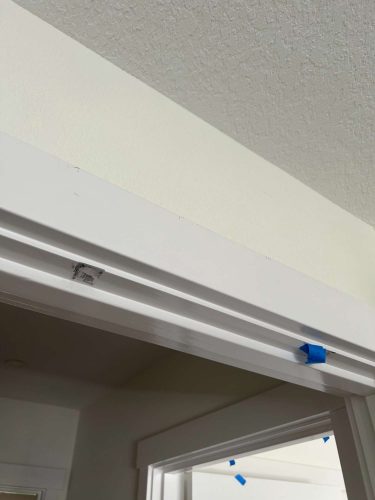 A close-up photo shows a painted white interior door frame in Arnold, May 2025. Blue painter’s tape and a patch of spackle are visible above the doorway, likely marking spots for touch-ups by painters or painting contractors.