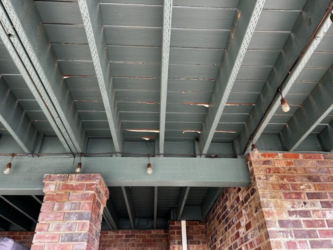Damaged wooden deck ceiling with cracks, supported by brick columns and string lights, at the Anderson ext in Portland. Suitable for inspection or repair by a painter, such as Pearl Painters. June 2025.