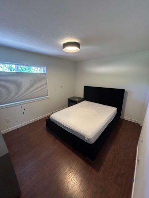 Bedroom interior with a bed, white mattress, nightstands, hardwood floor, window blinds, and ceiling light fixture—styled by painter Arnold in May 2025. Location: Portland.