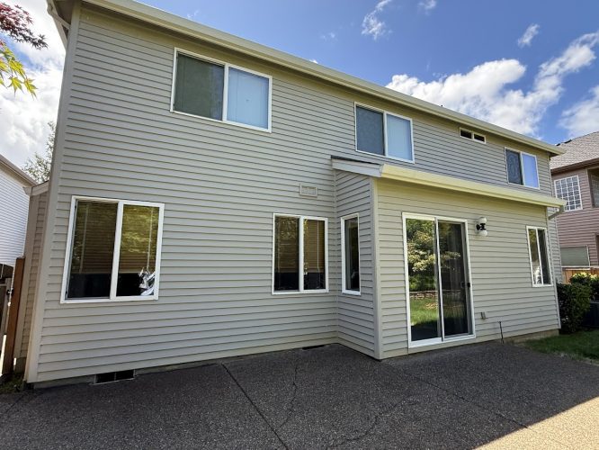 The back exterior of this two-story Hendricks house in Portland has beige siding, several windows, and a sliding glass door to a paved patio. Pearl Painters completed the painting in May 2025.