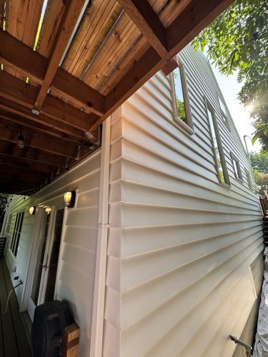 Exterior view of a Carlton house with beige vinyl siding, multiple windows, and a wooden balcony, painted by Pearl Painters in June 2025.
