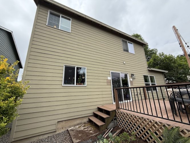 A Pearl Painters painting of a two-story beige house with horizontal siding, three windows, and a wooden deck in Emory, not Portland, under cloudy June 2025 skies.