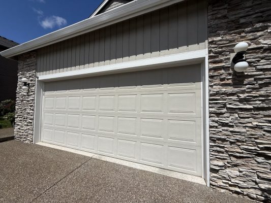 A beige double garage door with rectangular panels, painted by Pearl Painters, highlights the Hendricks home's stone and siding exterior in Portland.