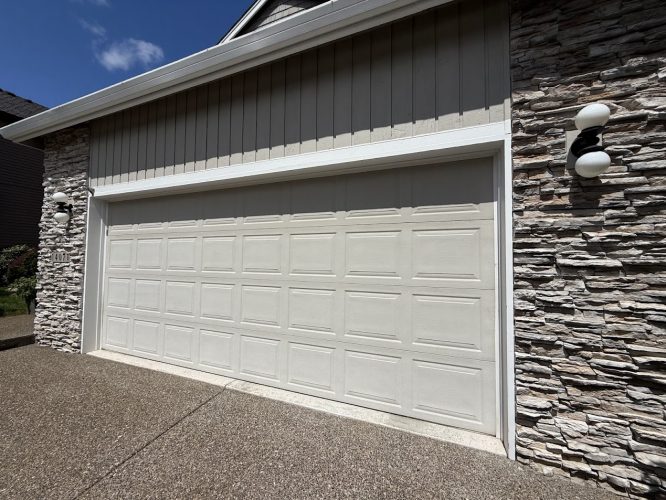 A beige double garage door with rectangular panels, painted by Pearl Painters, highlights the Hendricks home's stone and siding exterior in Portland.