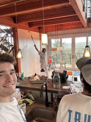 Three painters painting a modern wooden house interior in Portland; supplies on counter, one taking a selfie. Pearl Painters.
