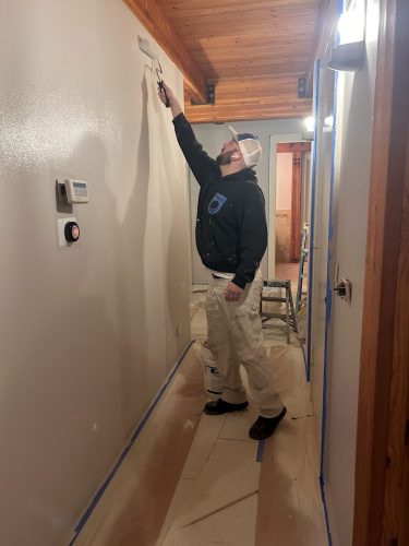 A painter from Pearl Painters paints a hallway wall in Portland, using a roller; floor has sheets and tape on the edges.