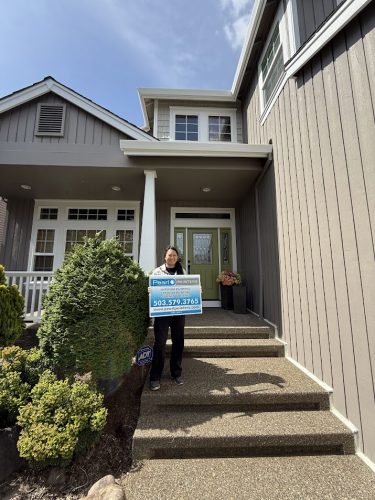 A painter stands on the front steps of a modern Hendricks house in Portland, holding a real estate sign, May 2025. Pearl Painters.