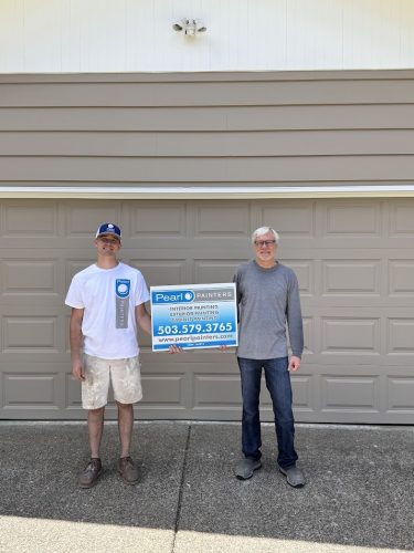 Two painters hold a Pearl Painters sign with contact info in front of a garage door in Cleveland; now booking exterior painting.