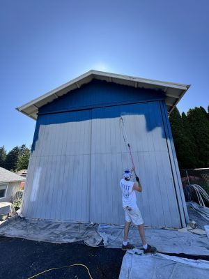 Painter uses roller on tall building exterior, July 2025; Deppe drop cloths cover ground. Pearl Painters, Portland.