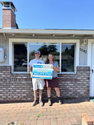 Two people in front of a house hold a Pearl Painters painting promo sign with contact info, likely in Portland, July 2025 special.
