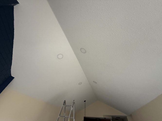 This photo shows a vaulted ceiling with four recessed lights, part of a dark-painted wall, a ladder, and a ceiling fan in an interior painted by Pearl Painters in Portland.