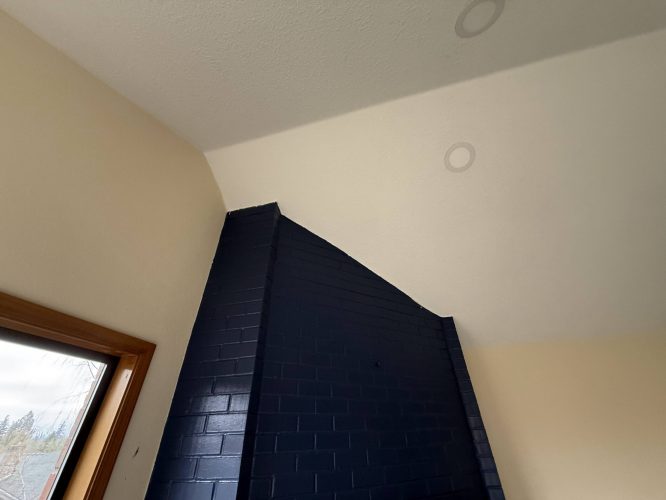 A dark blue brick chimney extends to a slanted white ceiling in this Yates interior in Portland, with cream walls and a wooden-framed window. Painted by Pearl Painters.