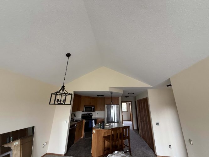 Photo of a modern Yates kitchen in Portland with light wood cabinets, stainless steel appliances, island seating, and vaulted ceilings with pendant lights. Painted by Pearl Painters. April 2025.