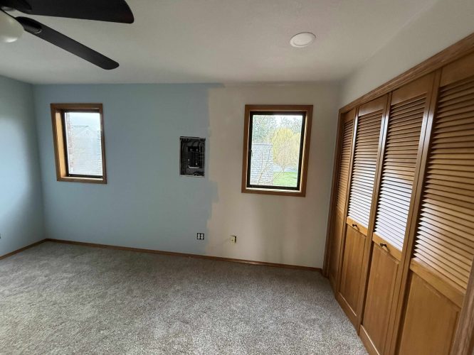 In April 2025 at Yates (outside Portland), a painter from Pearl Painters worked on a light blue interior room with two windows, a ceiling fan, carpeted floor, wood closet doors, and an unfinished paint area around the electrical panel.