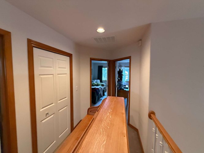 This hallway features a wooden handrail, white closet doors, and open doors to furnished rooms. Painting by Mann, April 2025. Inspiration for Portland interiors from Pearl Painters.