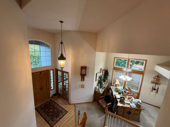 Interior of a house foyer and dining area in Portland, painted by Mann in April 2025. Features include a wooden front door, hanging light fixture, large windows, and a dining table with chairs. Pearl Painters.