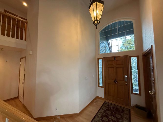 Interior entryway painting by Pearl Painters, Portland; features a wooden front door with sidelights, arched window above, lantern light fixture, wood floors, and partial staircase view. Painted by Mann, April 2025.
