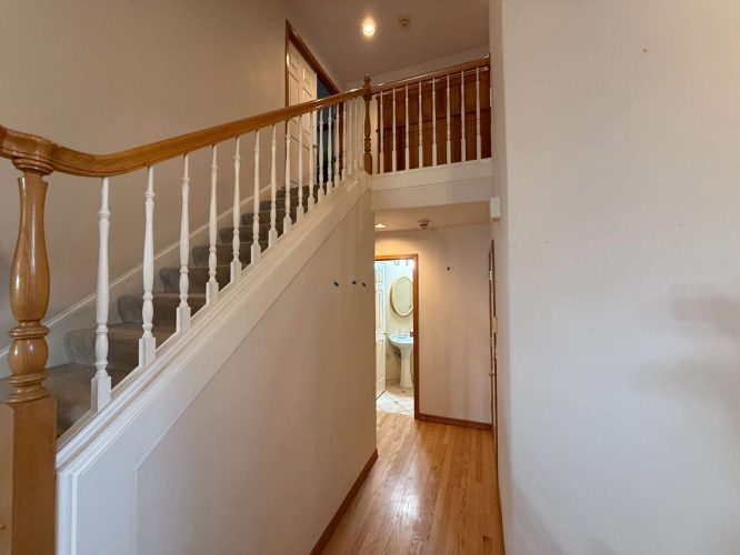 A freshly painted interior hallway in Portland features a staircase with a wooden railing and leads to an updated bathroom with a round mirror, showcasing April 2025 design trends. Painted by Pearl Painters.