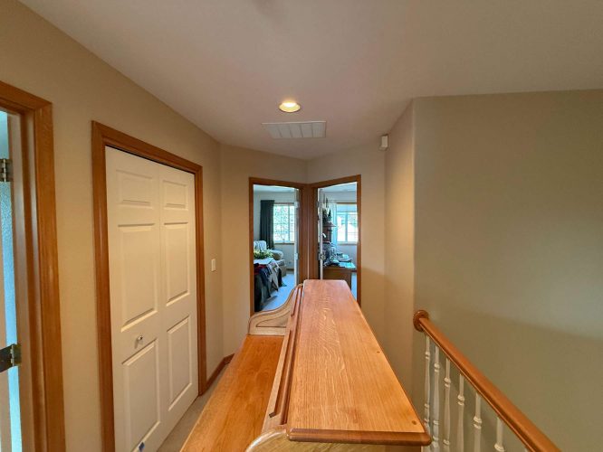 A hallway in a Mann home, Portland: beige-painted walls, white closet door, wood railing, and view into a furnished bedroom. Pearl Painters completed the painting for April 2025.