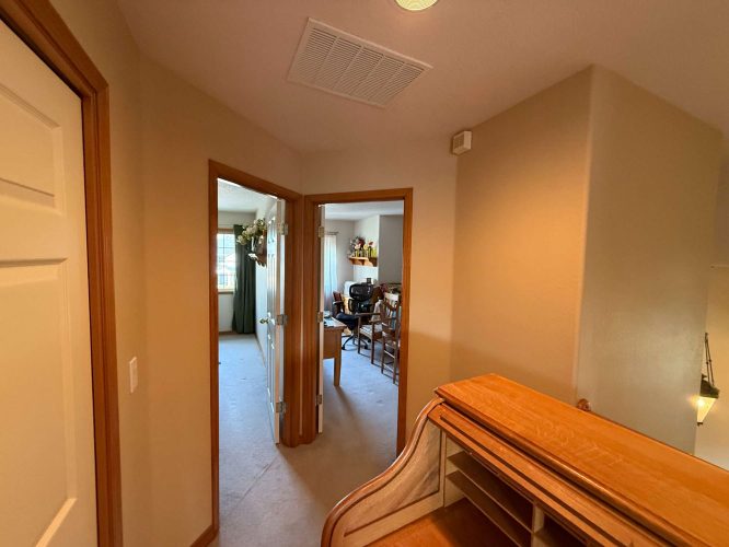 A hallway with beige walls, painted by Pearl Painters in Portland, leads to two rooms: one with a wooden desk and chairs, and another with a window and curtains. The painting creates an inviting interior.