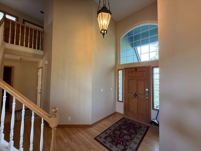 Painted by Mann in April 2025, this interior entryway in Portland features a wooden front door with sidelights, an arched window, a hanging light fixture, hardwood floors, and a staircase with white spindles. Pearl Painters is mentioned as the painting company.