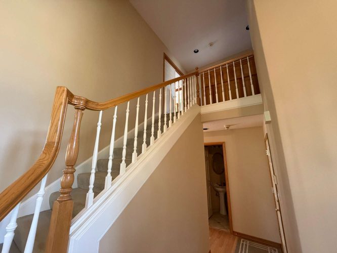 Interior staircase with wooden handrails and white balusters leading to an upper landing, with a small bathroom beneath the stairs. Painted by Pearl Painters, Portland, April 2025.