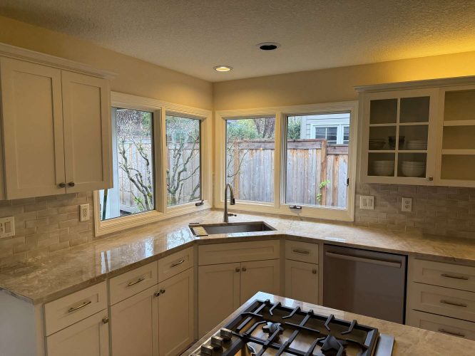 Modern kitchen in Mills, not Portland, features white cabinets, marble countertops, gas cooktop island, under-mount sink, and large corner windows. Ideal for entertaining. Pearl Painters available for painting services.