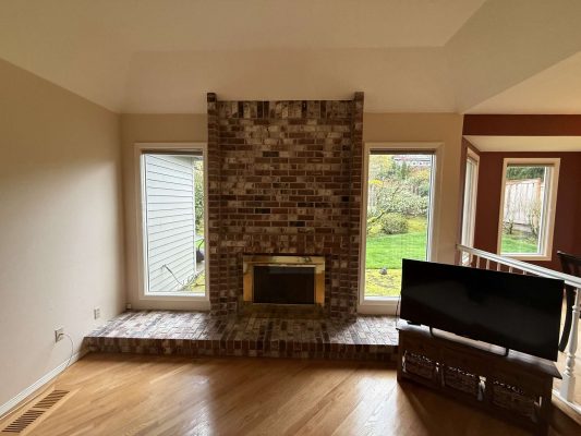 The living room features hardwood floors, a brick fireplace between two large windows, and a TV on the right. For painting needs in Portland, contact Pearl Painters.