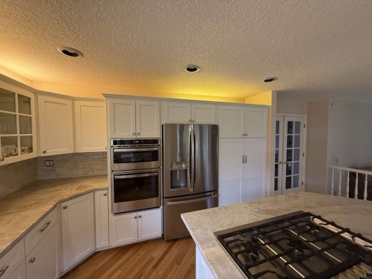 Modern kitchen painting in Portland: white cabinets, stainless steel double oven, refrigerator, and gas cooktop on island under recessed lighting. Painted by Pearl Painters for Mills listings, April 2025.