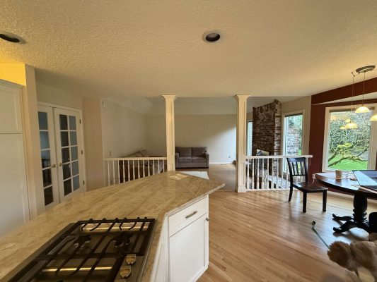 This Mills home in Portland features an open living area with a kitchen island, gas cooktop, hardwood floors, sofa, and large windows facing the backyard. Pearl Painters can help refresh your interior painting for April 2025.