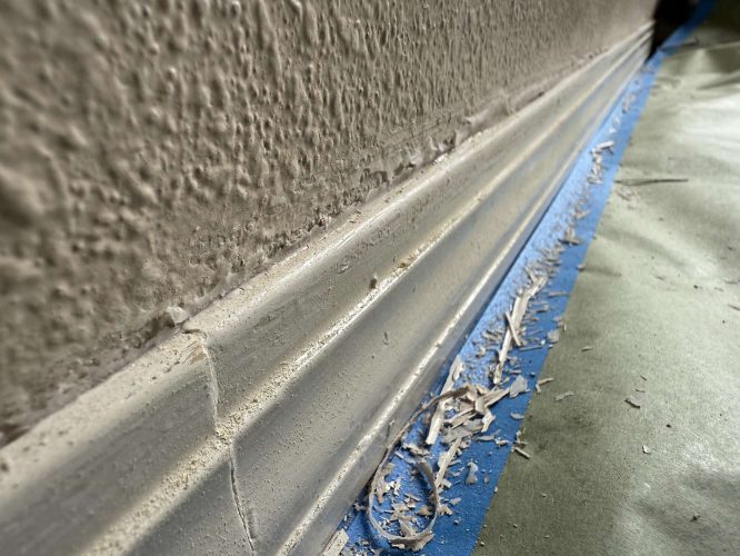 Close-up of a painted baseboard by painter Mills, April 2025, in Portland. Paint chips and debris are visible on painter’s tape and protective paper along the floor edge.
