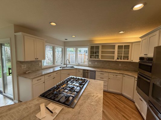 Modern kitchen in Portland with white cabinets, center island, gas cooktop, double ovens, and large windows overlooking fenced Mills backyard. Available April 2025. Contact Pearl Painters for painting services.