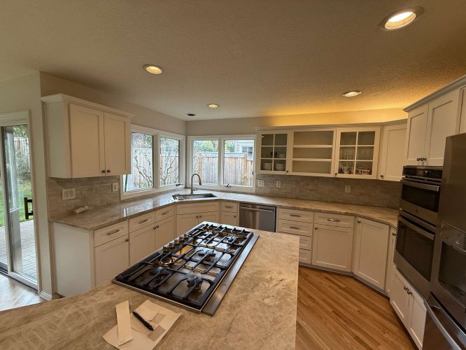Modern kitchen in Portland with white cabinets, center island, gas cooktop, double ovens, and large windows overlooking fenced Mills backyard. Available April 2025. Contact Pearl Painters for painting services.