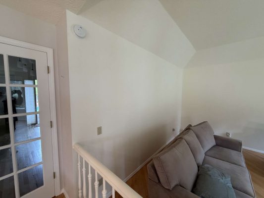 A painter in Portland shows a beige living room with a gray couch, white walls, an interior staircase railing, and Mills glass French doors—Pearl Painters' example for April 2025 decor trends.