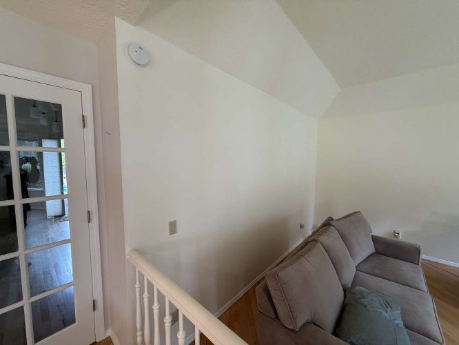 A painter in Portland shows a beige living room with a gray couch, white walls, an interior staircase railing, and Mills glass French doors—Pearl Painters' example for April 2025 decor trends.