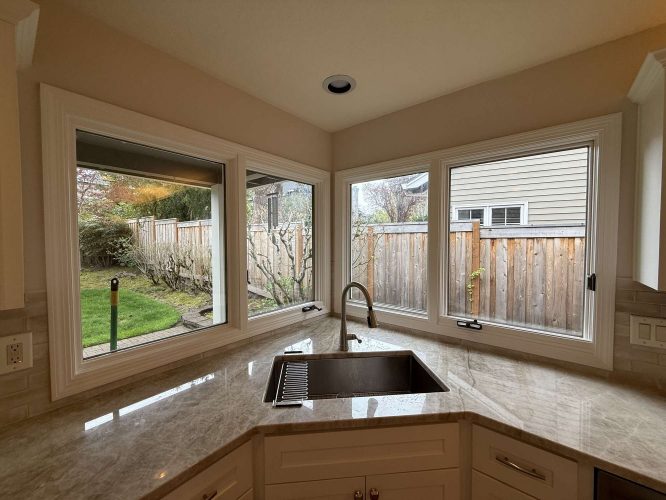 A Pearl Painters painting of a modern kitchen in Mills, Portland features a marble countertop, undermount sink, and large windows with views of a fenced backyard.