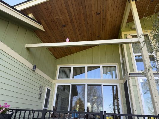 Photo of a green house in Portland with a wooden vaulted porch ceiling, large sliding glass doors, and black metal railing. Small birdhouse under the roof beam. Painted by Pearl Painters; photo taken April 2025 for McCaffery.
