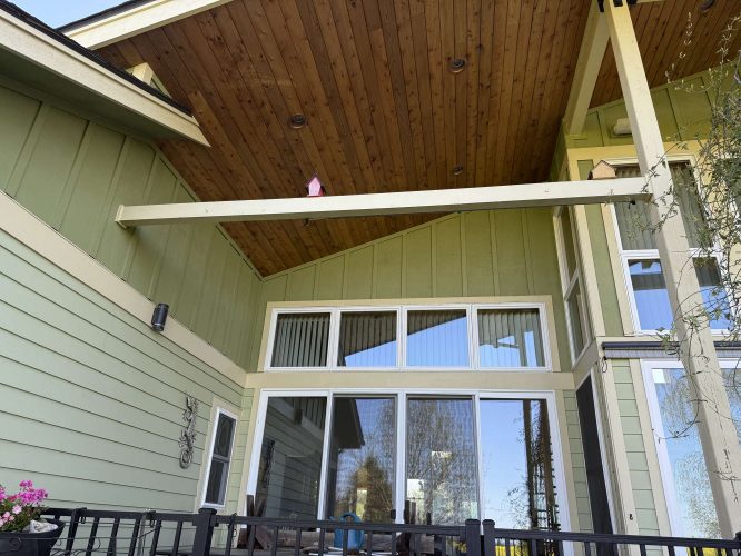 Photo of a green house in Portland with a wooden vaulted porch ceiling, large sliding glass doors, and black metal railing. Small birdhouse under the roof beam. Painted by Pearl Painters; photo taken April 2025 for McCaffery.
