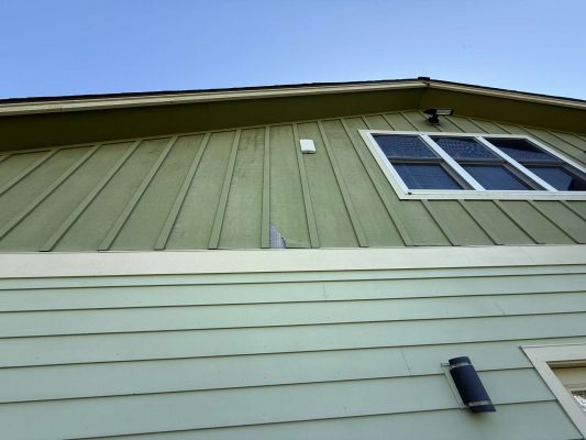 The image shows a green two-story house with a broken board, window, and two outdoor lights in April 2025 near McCaffery. The painting was likely done by Pearl Painters, a Portland painter.