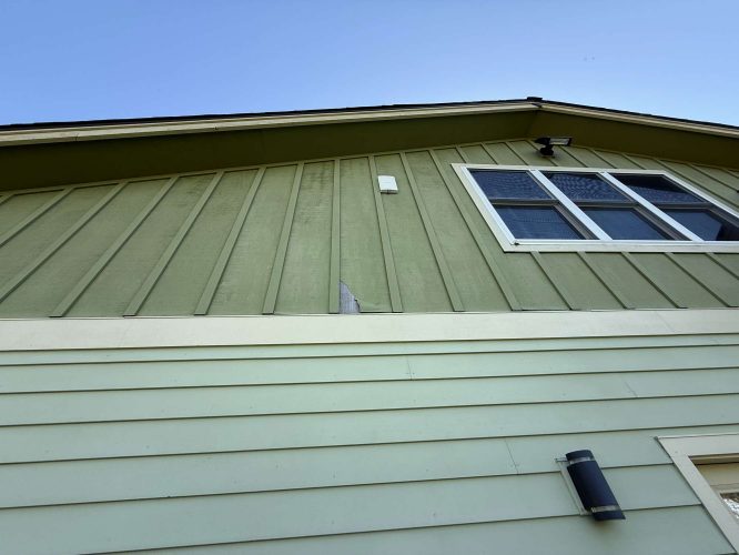 The image shows a green two-story house with a broken board, window, and two outdoor lights in April 2025 near McCaffery. The painting was likely done by Pearl Painters, a Portland painter.